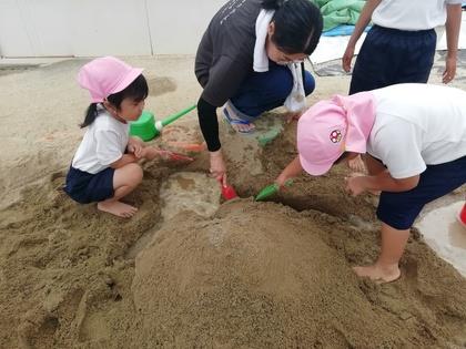 隣の友達が作った山とつなげようと、スコップで砂を掘って道を繋いでいます。