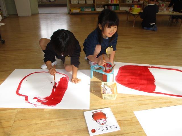 絵本を見て、だるまのイメージを広げ、白い画用紙に土台になる丸を大きく赤色の絵の具で描いています。