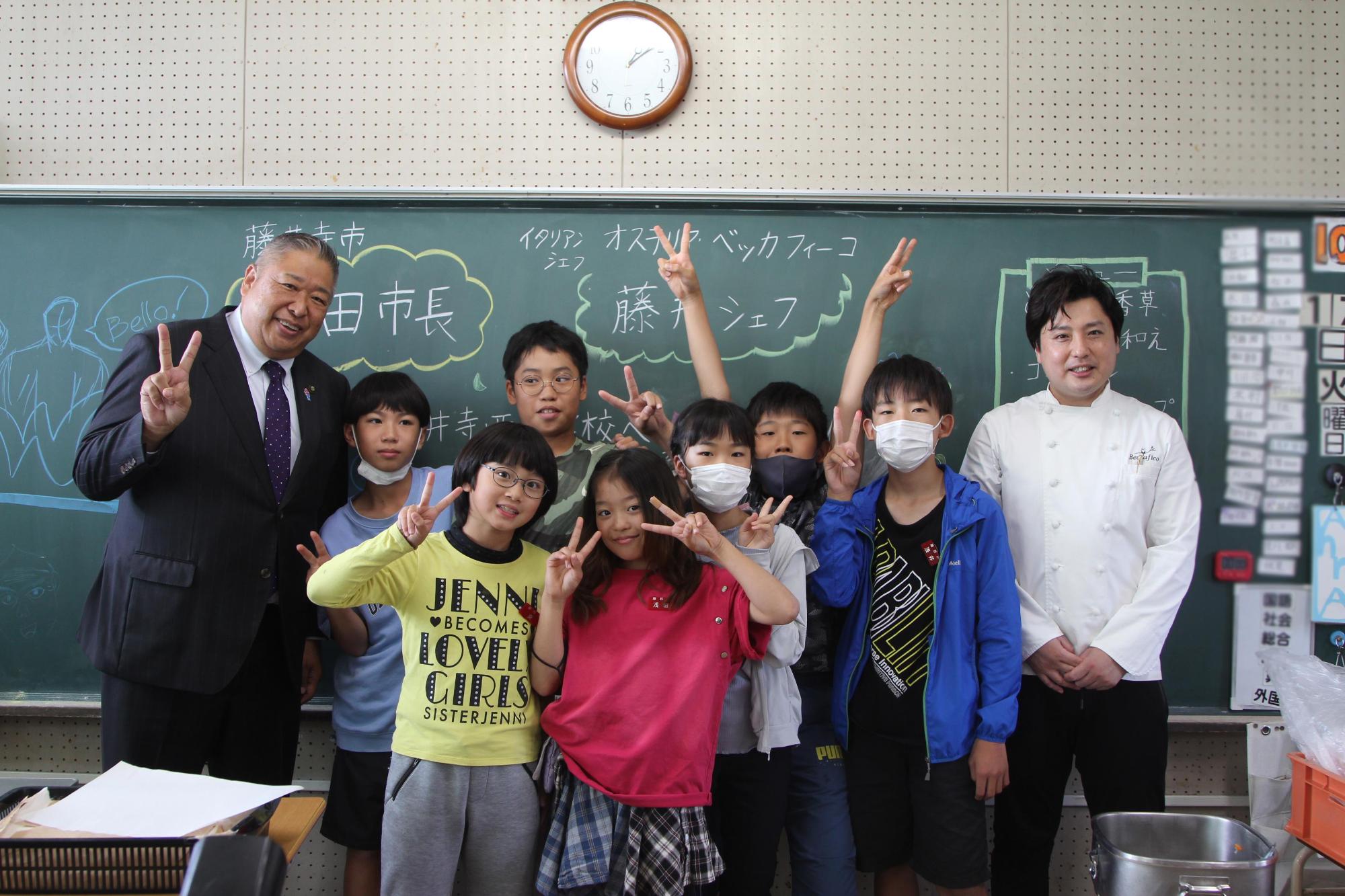 藤井シェフと岡田市長と子どもたちが教室の黒板の前で記念撮影する様子の写真