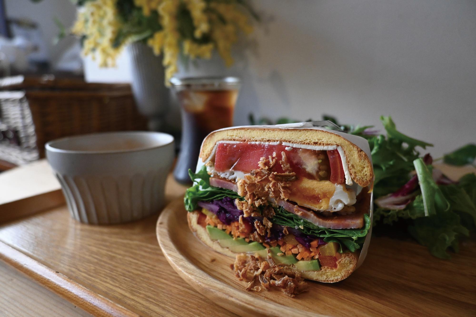 ベーコン＆エッグサンドイッチの写真（クラウドブレットの間にトマト・たまご・ベーコン・レタス・紫玉ねぎ・ニンジン・パプリカ・アボカドが挟まったヘルシーでボリューミーなサンドイッチ）の写真