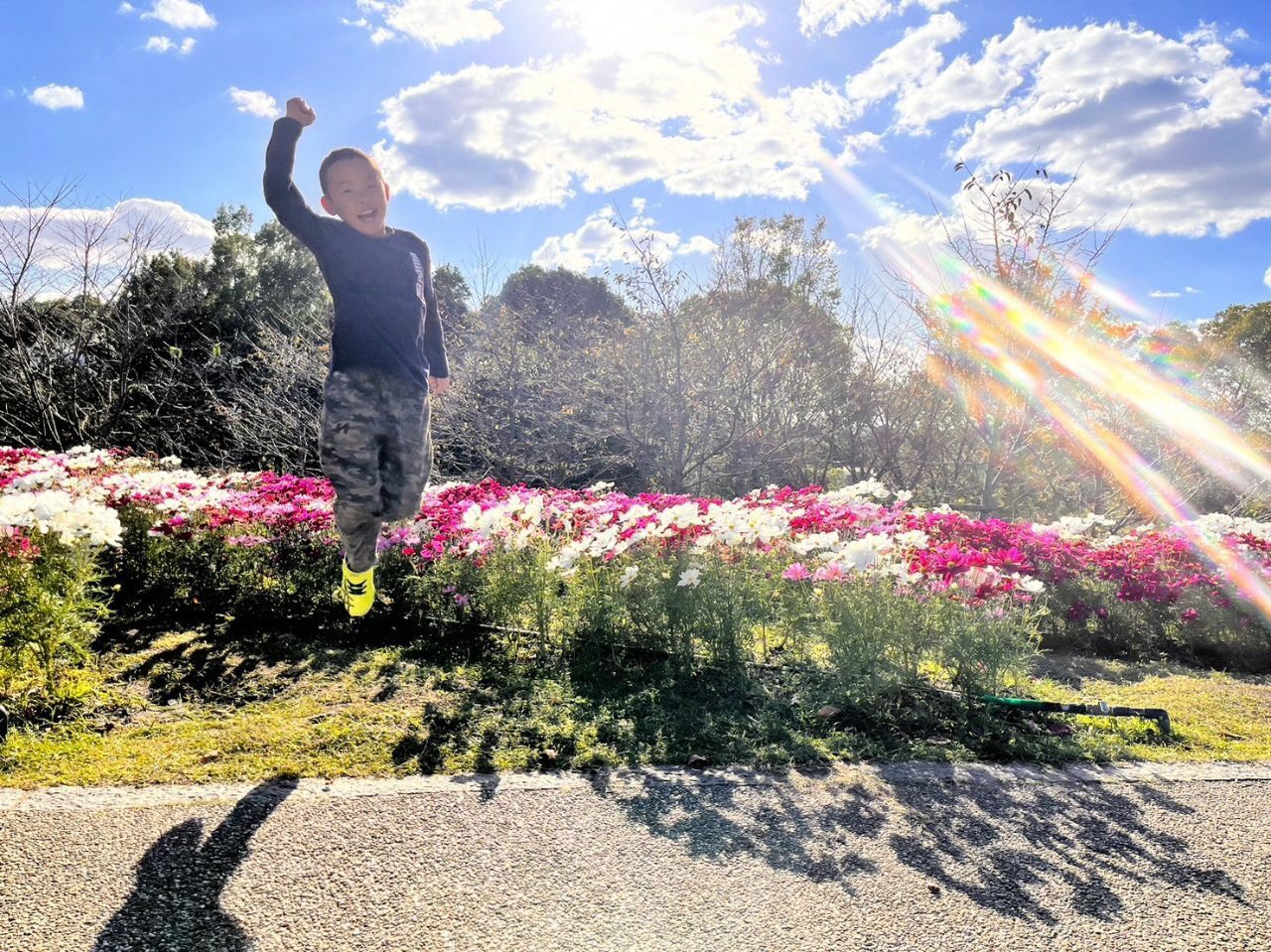 晴天の下、花畑の前で高くジャンプしているお子さんの写真