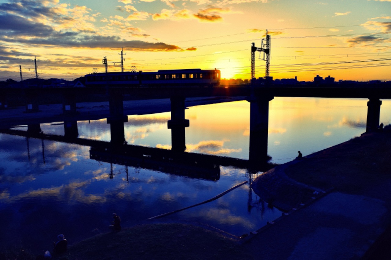 夕日と走っている電車が水面に反射して鏡のように映っている写真