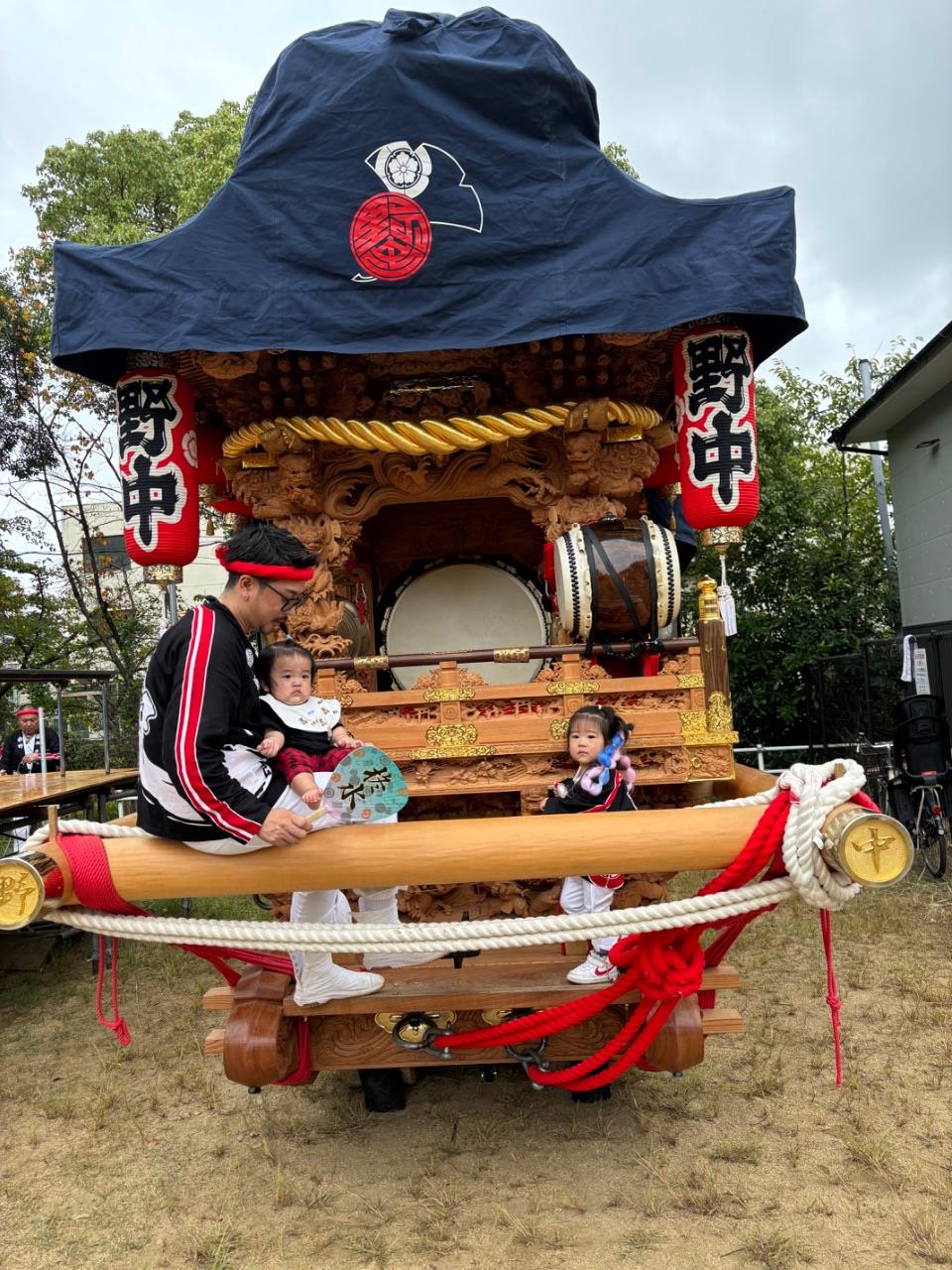 野中のだんじりの上に親子が座っている写真