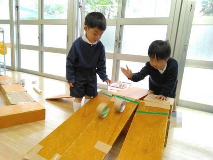 積み木をガムテープで止めて長いスロープを作って筒を転がして遊んでいます。