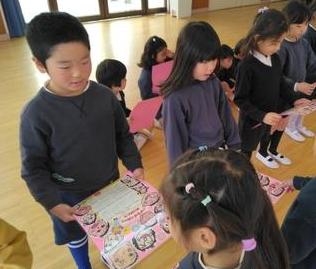 似顔絵付きのカレンダーのプレゼントを年少児が年長児に渡しています。