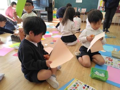 大きな画用紙をもって、サンタクロースの顔の輪郭を切っています。