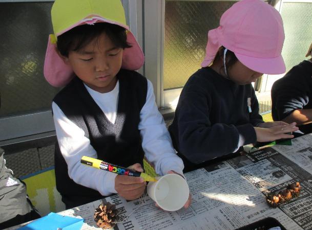 紙コップに紐でつないだまつぼっくりをつけて、けん玉を作っています。