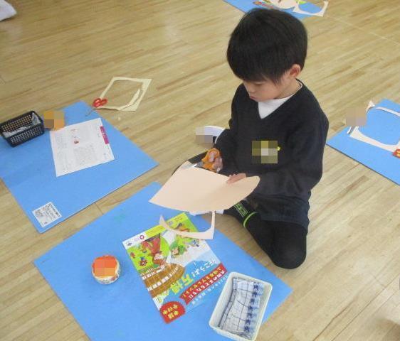画用紙にはさみを斜めに入れて大きな輪郭の丸を切っています。