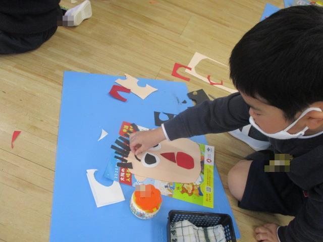画用紙を大きな山の形を切って、その下に小さな山の形を切って、眉毛を作っています。