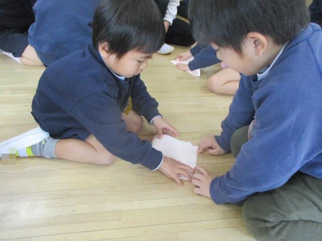 年長児が年少児に三方の折り方を優しく教えてくれています。